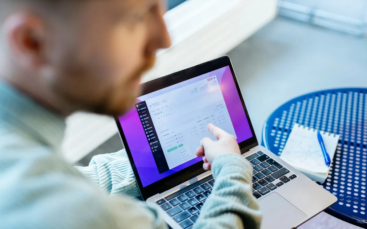 Business operator reconciling printed ledger sheets alongside a laptop to resolve manual record bottlenecks